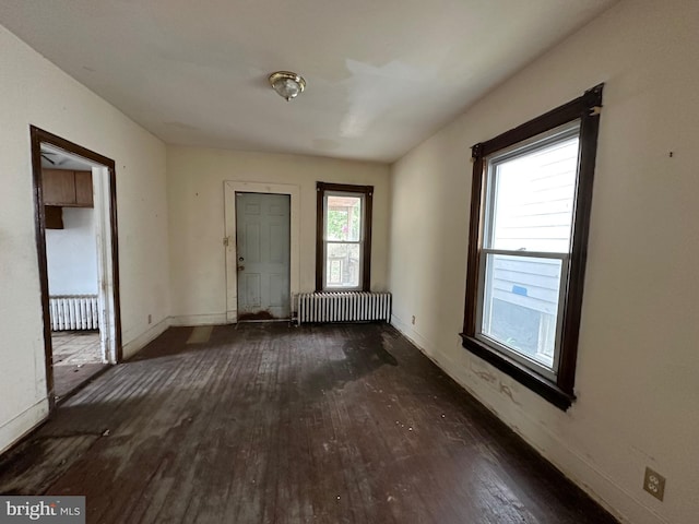 empty room with dark wood-type flooring and radiator heating unit