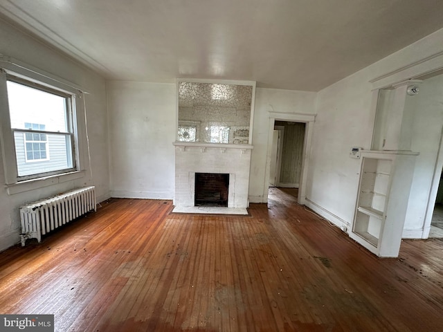 unfurnished living room with hardwood / wood-style flooring, radiator heating unit, and a brick fireplace