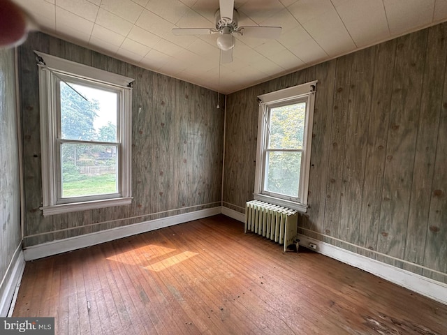 spare room with hardwood / wood-style flooring, radiator heating unit, wood walls, and ceiling fan