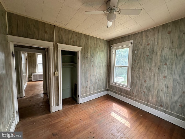 unfurnished bedroom with ceiling fan, wood walls, wood-type flooring, multiple windows, and a closet