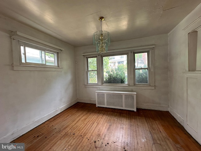 spare room with radiator, a wealth of natural light, a chandelier, and hardwood / wood-style flooring