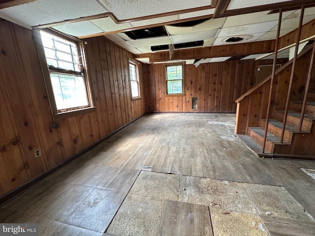 basement featuring a paneled ceiling and wooden walls