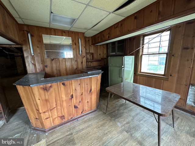 kitchen featuring kitchen peninsula, a paneled ceiling, wooden walls, and white refrigerator