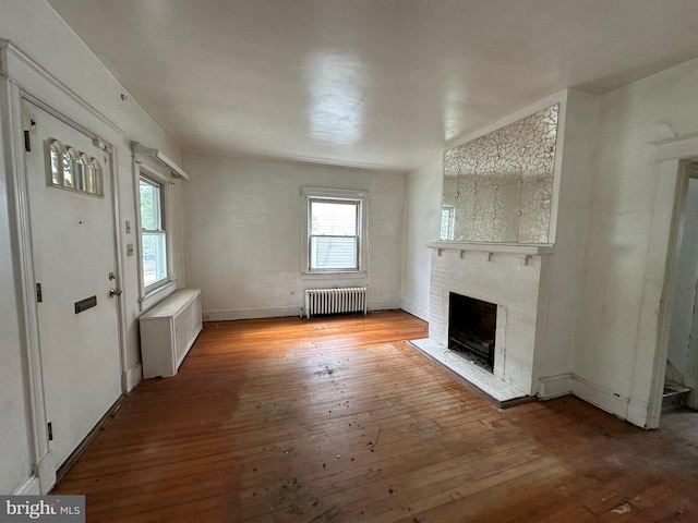 unfurnished living room featuring radiator, wood-type flooring, and a brick fireplace