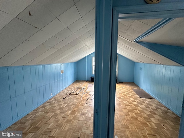 bonus room with vaulted ceiling, wood walls, and light parquet floors