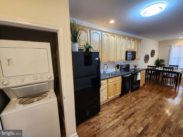 kitchen featuring black appliances, sink, stacked washer and clothes dryer, light brown cabinetry, and hardwood / wood-style flooring