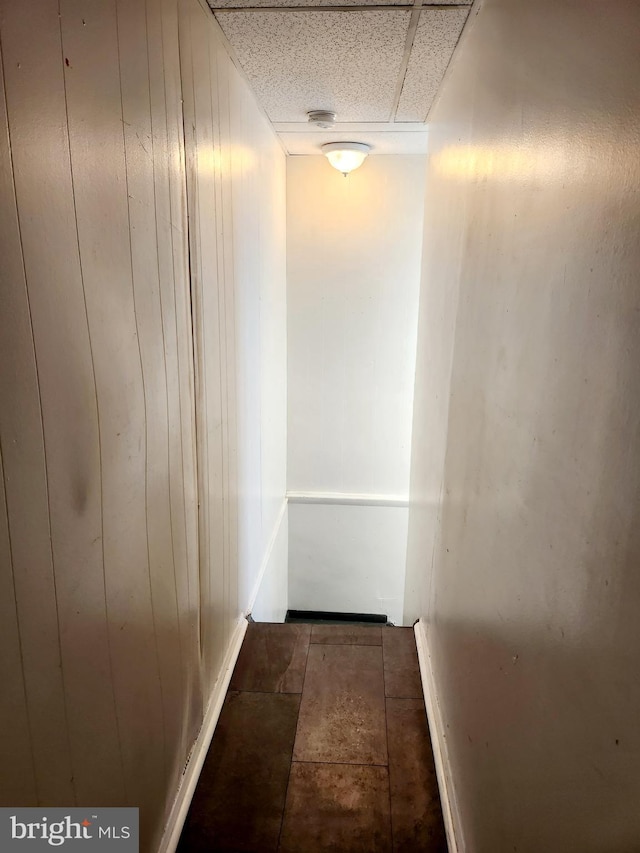 hallway featuring a drop ceiling and wood walls