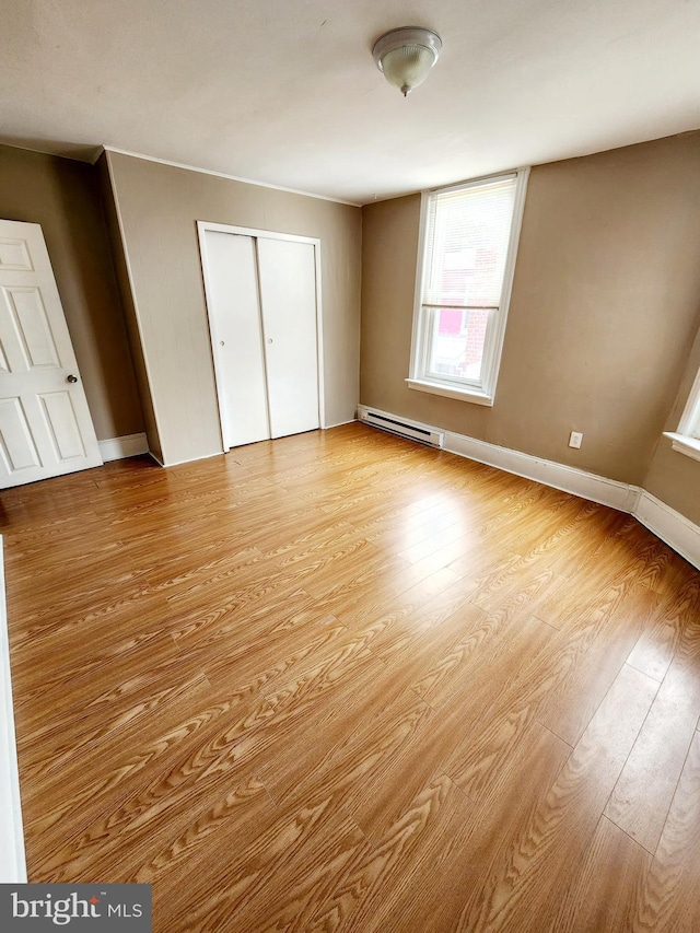 unfurnished bedroom with baseboard heating, a closet, and light hardwood / wood-style flooring