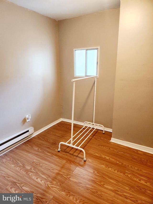 unfurnished room featuring hardwood / wood-style floors and a baseboard heating unit