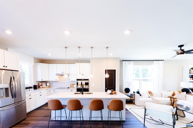 kitchen featuring white cabinetry, a kitchen breakfast bar, stainless steel fridge, pendant lighting, and a kitchen island with sink