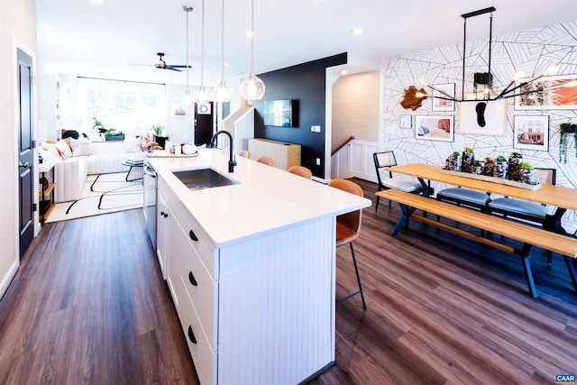 kitchen featuring a center island with sink, sink, white cabinets, and hanging light fixtures