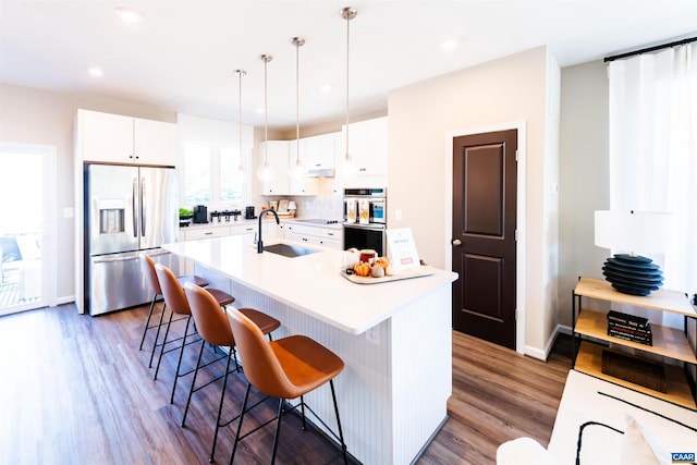 kitchen with white cabinets, a center island with sink, sink, hanging light fixtures, and stainless steel appliances