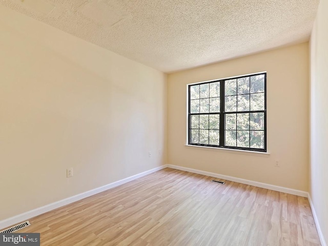 empty room with light hardwood / wood-style flooring, a textured ceiling, and a healthy amount of sunlight