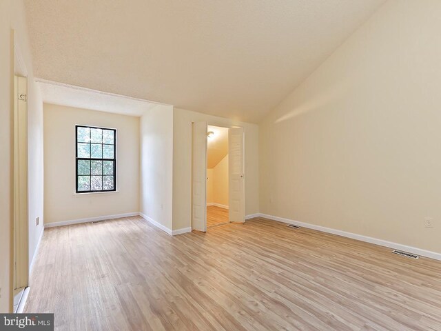 spare room with light wood-type flooring and vaulted ceiling