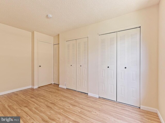 unfurnished bedroom with a textured ceiling, light hardwood / wood-style flooring, and two closets