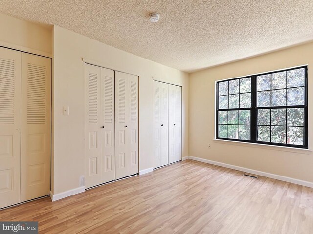 unfurnished bedroom with a textured ceiling, light hardwood / wood-style flooring, and two closets