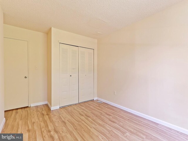 unfurnished bedroom featuring light wood-type flooring, a closet, and a textured ceiling