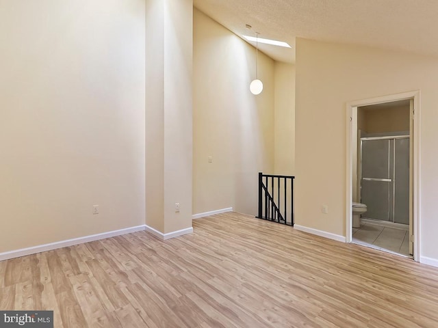 empty room with light hardwood / wood-style floors, vaulted ceiling, and a textured ceiling