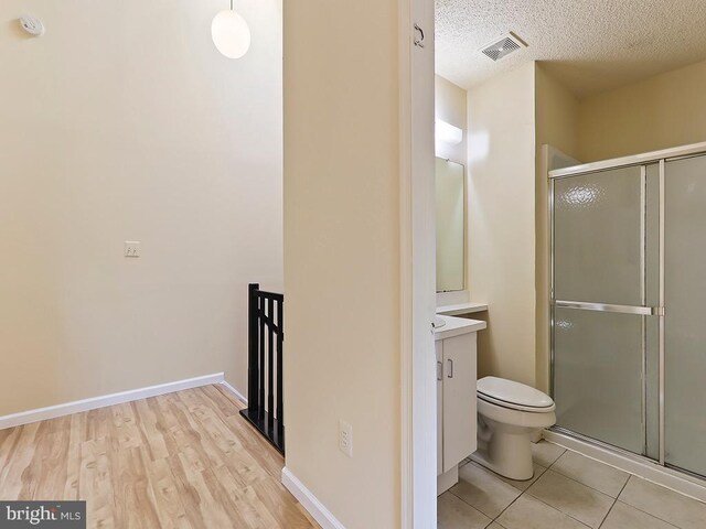 bathroom with hardwood / wood-style floors, a shower with shower door, a textured ceiling, vanity, and toilet