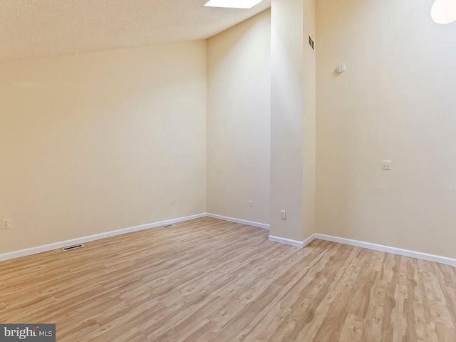 spare room with light hardwood / wood-style floors, vaulted ceiling, and a textured ceiling