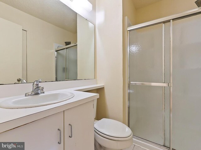 bathroom with tile patterned floors, a textured ceiling, vanity, toilet, and walk in shower