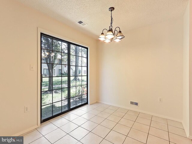 empty room featuring a textured ceiling, a chandelier, and light tile patterned floors