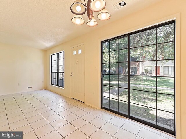 doorway featuring a textured ceiling, a notable chandelier, and light tile patterned flooring