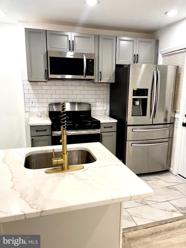 kitchen featuring gray cabinetry, light hardwood / wood-style flooring, decorative backsplash, and stainless steel appliances