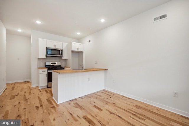 kitchen featuring kitchen peninsula, butcher block counters, stainless steel appliances, and white cabinetry