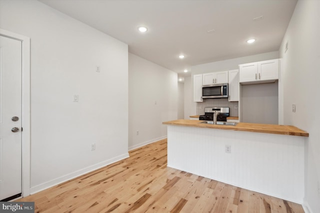 kitchen with decorative backsplash, wood counters, stainless steel appliances, and white cabinetry