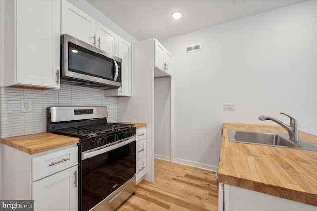 kitchen featuring white cabinets, appliances with stainless steel finishes, sink, backsplash, and butcher block countertops