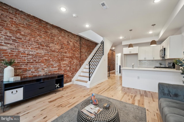 living room featuring sink, brick wall, and light wood-type flooring