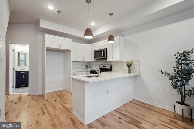 kitchen featuring kitchen peninsula, sink, hanging light fixtures, stainless steel appliances, and white cabinets