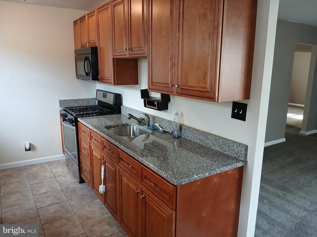 kitchen featuring light carpet, stainless steel range with gas stovetop, dark stone countertops, and sink