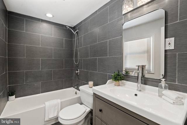 full bathroom with tile walls, tiled shower / bath combo, vanity, and toilet