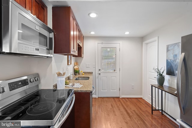 kitchen featuring light wood-type flooring, stainless steel appliances, light stone counters, and sink