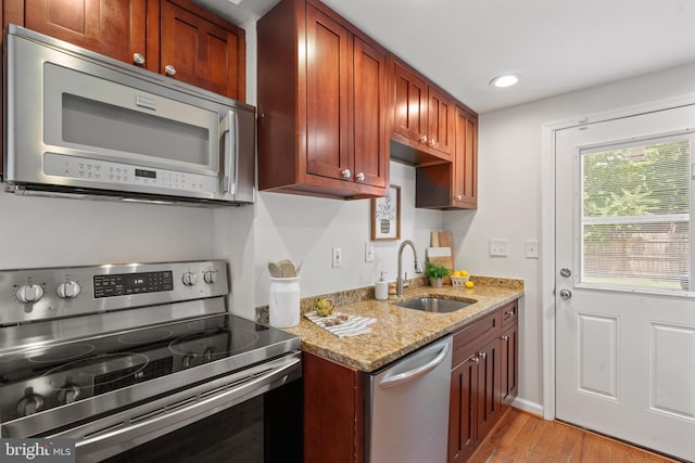 kitchen with light stone countertops, sink, stainless steel appliances, and light hardwood / wood-style floors