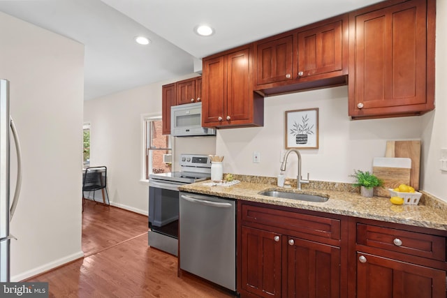 kitchen featuring appliances with stainless steel finishes, light hardwood / wood-style floors, light stone counters, and sink