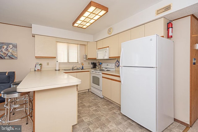 kitchen with white appliances, cream cabinets, sink, a kitchen bar, and kitchen peninsula