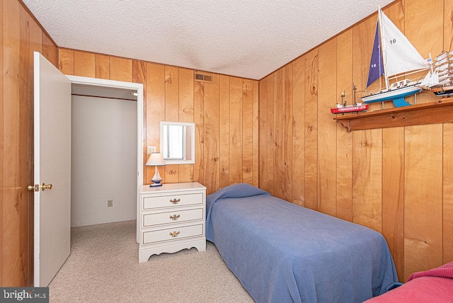 bedroom featuring a textured ceiling, light carpet, and wooden walls