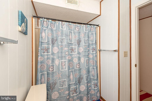 bathroom featuring a textured ceiling and wood walls