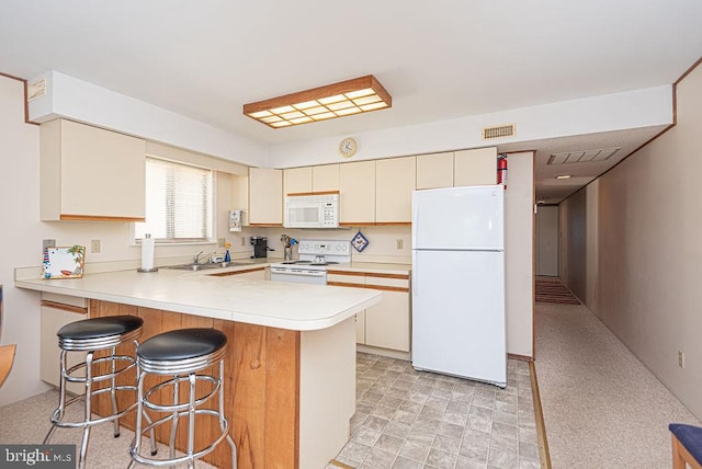 kitchen with a kitchen bar, kitchen peninsula, white appliances, and cream cabinetry