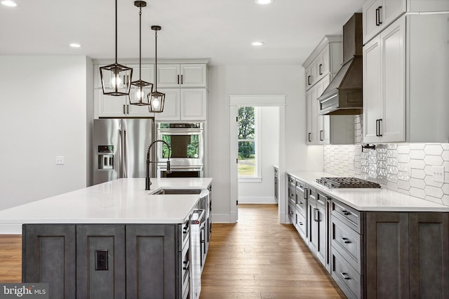 kitchen featuring light hardwood / wood-style flooring, pendant lighting, a center island with sink, appliances with stainless steel finishes, and custom exhaust hood