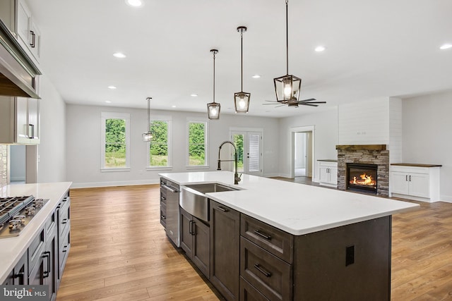 kitchen with light wood-type flooring, ceiling fan, sink, a fireplace, and an island with sink