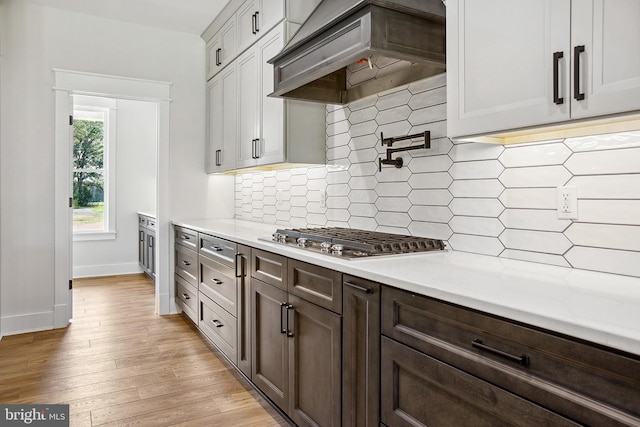 kitchen with premium range hood, white cabinets, decorative backsplash, light hardwood / wood-style floors, and stainless steel gas cooktop