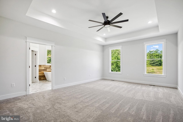 spare room with ceiling fan, light colored carpet, and a tray ceiling