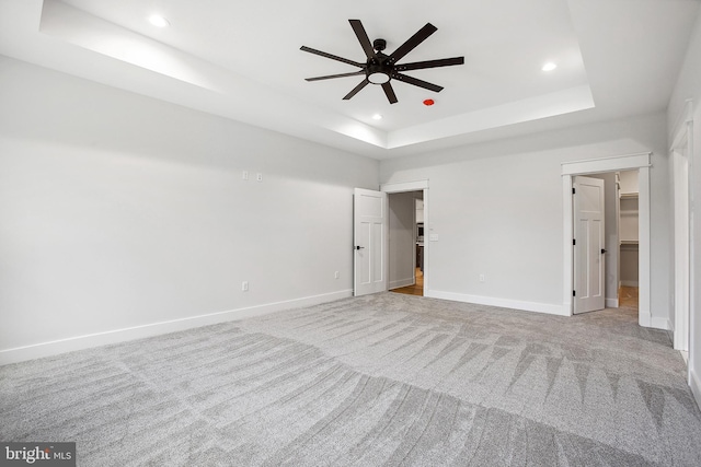 unfurnished bedroom with a tray ceiling, a spacious closet, ceiling fan, and light carpet