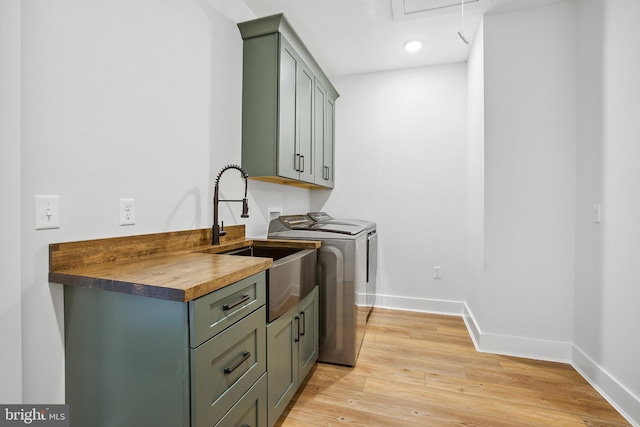 clothes washing area with washing machine and dryer, sink, cabinets, and light wood-type flooring