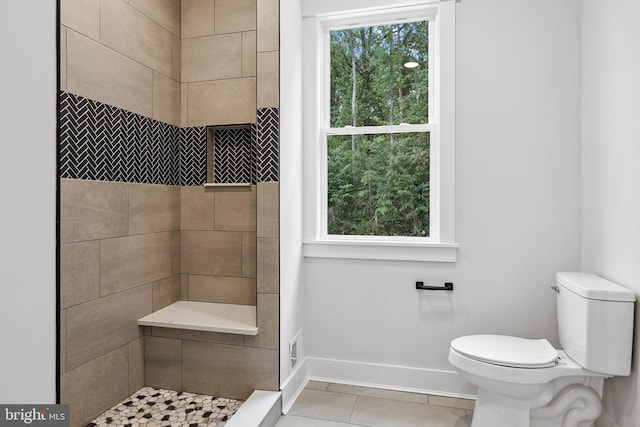 bathroom with toilet, a tile shower, and tile patterned floors