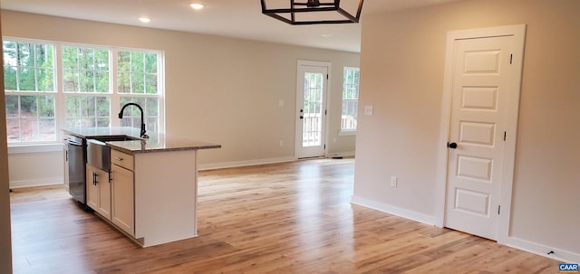 kitchen with dark stone countertops, light wood-type flooring, plenty of natural light, and a center island with sink